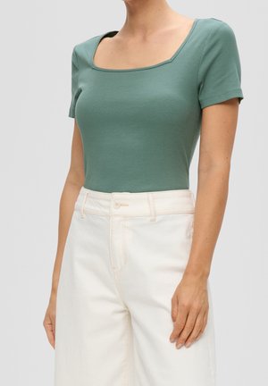 Vihreä ribbikuvioinen lyhythihainen toppi, jossa on neliökaula-aukko, yhdistettynä korkeavyötäröisiin kermaisiin leveälahkeisiin housuihin. Teksturoitu kangas, istuva muotoilu.