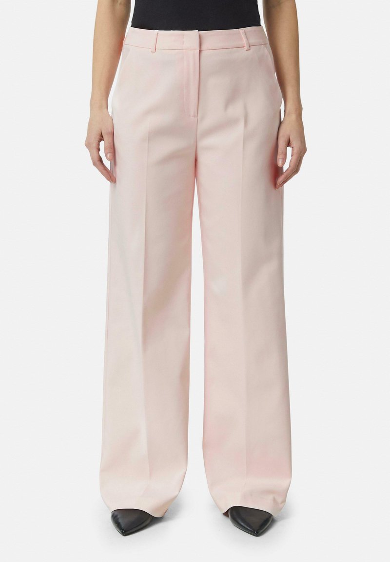 Helle rosa weite Hosen aus glattem Stoff. Mit einer mittigen Falte, Gürtelschlaufen und einem Reißverschluss vorne. Schwarze spitz zulaufende Schuhe.