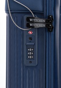Valise rigide marine avec des rainures verticales, un cadenas à combinaison et des zips de marque. Comprend une fente de sécurité approuvée par la TSA.