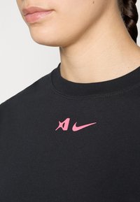 Black cotton T-shirt with a crew neck, featuring a pink Nike logo on the chest and a textured fabric. Simple, clean design.