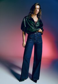 Veste bomber en cuir noir avec une silhouette ajustée, associée à un jean en denim noir à taille haute et jambes larges, et des escarpins à bout pointu.