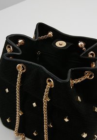 Borsa a secchiello in suede nera con catene in tonalità oro, dettagli borchiati, chiusura a coulisse e tasca interna con zip.