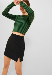 Zeleno-černý pruhovaný crop top v kombinaci s černou mini sukní se bočním rozparkem. Top má dlouhé rukávy a obepínající střih.