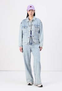 Chaqueta de mezclilla azul claro y jeans de corte holgado a juego, combinados con una gorra lavanda con bordado de rosa. Ajuste casual y relajado.