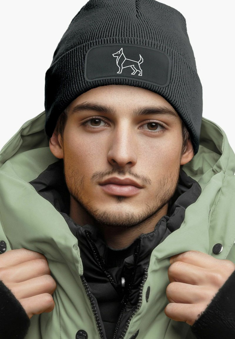 Black knit beanie with a dog logo patch, worn with a light green puffer jacket, featuring a zippered front and hood, layered over a black inner garment.