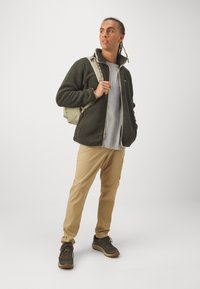 Fleecejakke i mørkegrøn, grå t-shirt, tan bukser og grå vandresko. Rygsæk med lyse beige detaljer. Glatte teksturer og afslappet pasform.