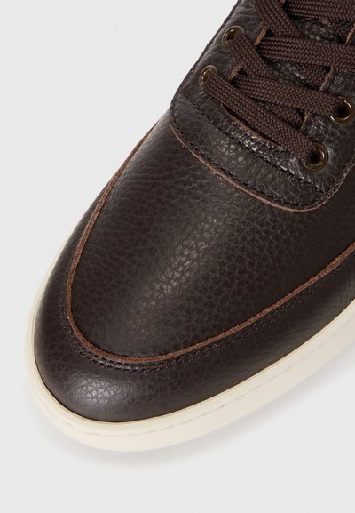 Brown leather sneaker with a textured upper, contrasting brown stitching, and round laces. Cream-colored rubber sole and metal eyelets.