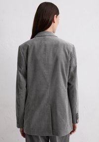 Gray tailored blazer with a structured design, notched lapels, and buttoned cuffs, featuring a smooth fabric texture and vented back.