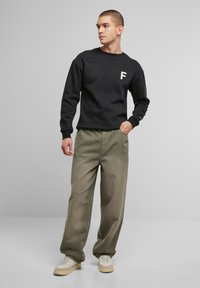 Mustmust navi valge "F" logoga, koos lahtiste oliivroheliste pükste ja beezide tossudega. Riiete kangatekstuurid on nähtavad.