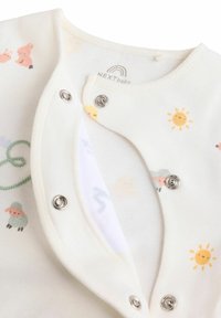 Bomuld baby body i creme med trykknapper, med et mønster af får, kaniner og soler i pastelfarver. Blødt, tekstureret stof.
