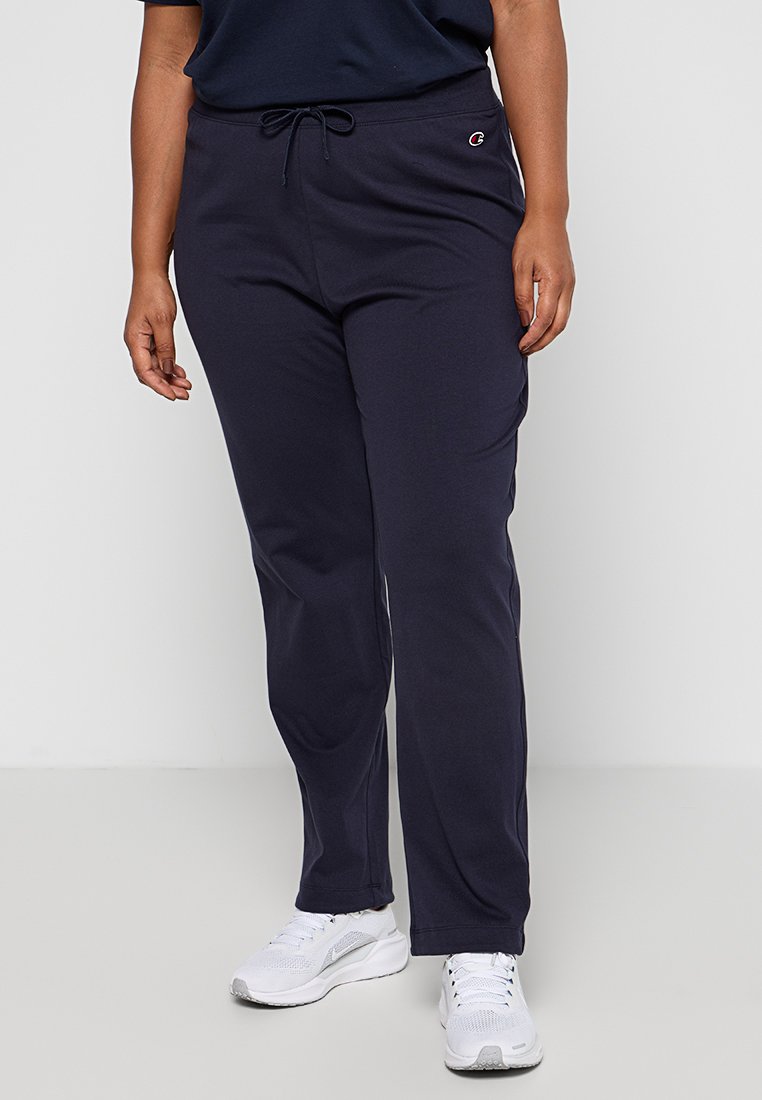 Pantalons de jogging bleu marine en tissu doux, avec une taille élastique à cordon de serrage et des poches latérales, assortis à des chaussures de sport blanches.