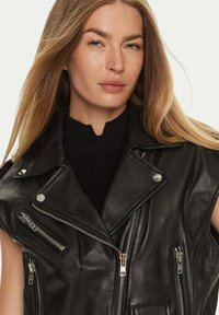 Zwarte leren vest met een gekartelde kraag, meerdere ritszakken en zilveren hardware accenten. Gladde textuur en mouwloos ontwerp.