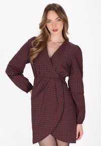 Robe portefeuille à carreaux rouges et verts avec de longues manches bouffantes, décolleté en V et ourlet asymétrique, fabriquée à partir d'un tissu lisse.
