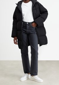 Black puffer coat with a hood, zip closure, and quilted texture, paired with high-waisted dark jeans and white sneakers.