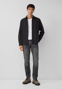 Grijze overhemd met knopen over een wit T-shirt, gedragen met donkere jeans en bruin veterlaarzen. Het overhemd heeft een borstzakje.