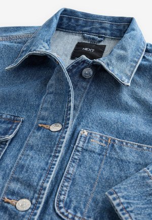 Helles blaues Denimhemd mit klassischem Kragen, vorderem Knopfverschluss, zwei Brusttaschen und silbernen Beschlägen. Abgestumpfte Textur und Nähdetails.