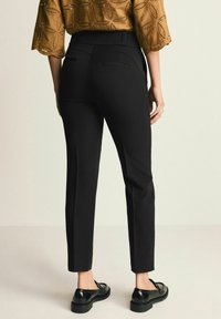 Schwarze maßgeschneiderte Hose mit schmaler Passform, ausgestattet mit einer glatten Textur und seitlichen Nahttaschen, kombiniert mit schwarzen Schuhen für einen Kontrast.