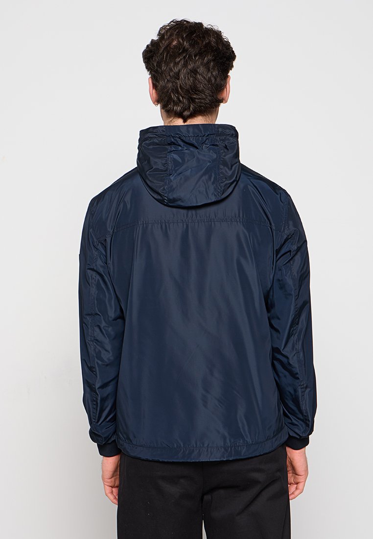 Dunkelblaue Jacke mit Kapuze. Aus leichtem, glänzendem Material gefertigt. Verfügt über elastische Bündchen und eine lockere Passform mit einer glatten Textur.