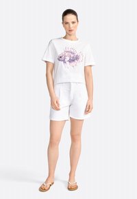 Tricou alb din bumbac cu un design colorat de pește, asociat cu pantaloni scurți albi din in și flip-flops bej. Croială casual, relaxată.