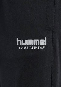 Zwarte sportkledingstof met een wit "hummel" logo en "SPORTSWEAR" tekst; gladde textuur met een aansluitend ontwerp.