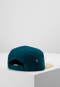 Türkiser Stoffhut mit einem hellbraunen Schirm, Sechseck-Design, Metallösen und verstellbarem Riemen auf der Rückseite. Mattes Finish.