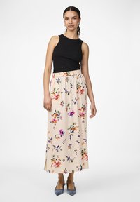 Un haut sans manches noir associé à une jupe maxi beige à fleurs ornée de motifs colorés et d'une fente sur le côté, complétée par des escarpins bleu clair.