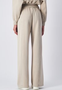 Pantaloni da tuta larghi beige con vita elasticizzata, caratterizzati da cuciture a vista, texture morbida e vestibilità comoda. Ideali per un look informale.