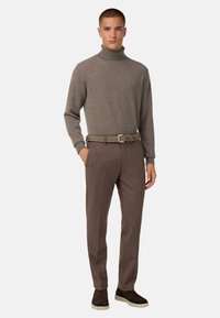 Hnědý rolák, přiléhavý, s jemnou texturou. Hnědé kalhoty na míru s jemným vzorem. Tkaný opasek a tmavé slip-on boty dotvářejí vzhled.