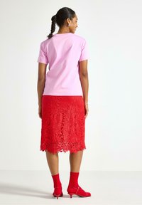 Lyserød bomulds t-shirt med korte ærmer, parret med en rød blonde-nederdel med blomster mønstre, røde sokker og åbne røde hæle.