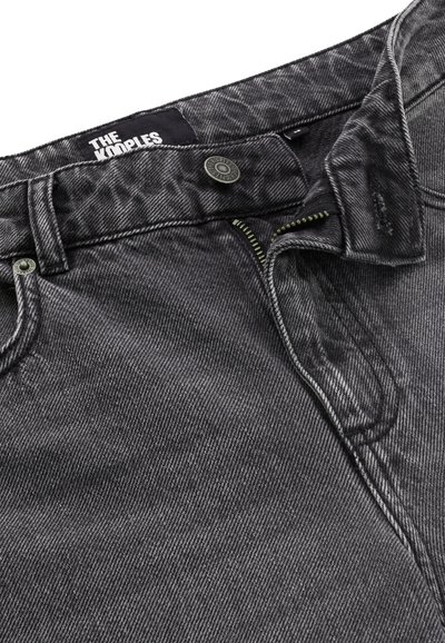 Pantalones de mezclilla negros con un acabado desgastado. Presentan un cierre a botón, cremallera y costuras en contraste. La etiqueta dice "THE KOOPLES."