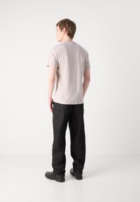 Camiseta de manga corta gris claro con escote redondo, combinada con pantalones de mezclilla oscuros y calzado negro, vista desde la espalda.