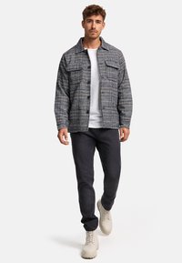 Light gray and dark blue plaid jacket with two chest pockets, paired with a white t-shirt and dark jeans. Beige lace-up boots complete the look.