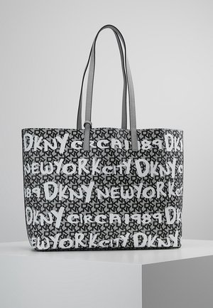 Czarno-biała torba DKNY typu tote z powtarzającym się logo, napisami „New York City” i „Circa 1989”, posiadająca dwa szare paski na ramię.