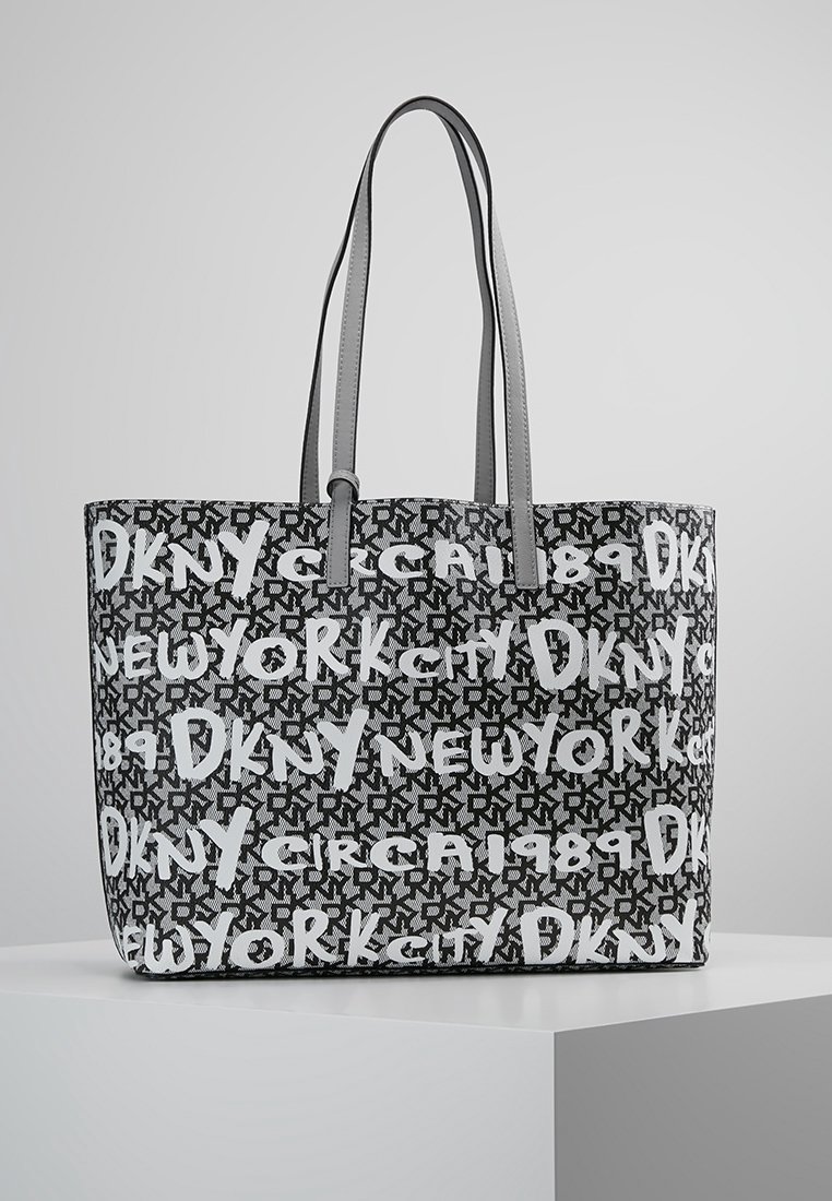 Sac cabas DKNY noir et blanc avec logo répété, texte « New York City » et « Circa 1989 », avec deux anses d'épaule grises.