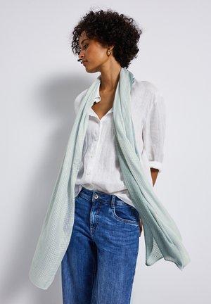 Scarf azzurro chiaro, texture morbida, appoggiato su una camicia bianca con bottoni, abbinato a jeans di denim blu. Il foulard presenta un motivo a quadri delicato.
