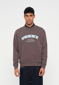 Tmavofialová mikina so stojatým golierom, s potlačou "TOMMY JEANS New York City" v svetlom modrom a bielom, s rebrovanými manžetami a lemom.
