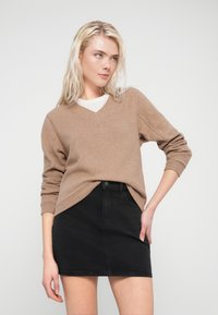 Pull beige en maille avec un col en V, associé à une mini-jupe en denim noir. Le pull présente une texture côtelée et des manches longues.