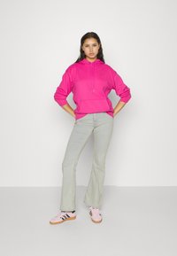 Felpa rosa con cappuccio e tasca frontale, abbinata a jeans grigi chiari a zampa d'elefante. Footwear presenta camoscio rosa con accenti neri.