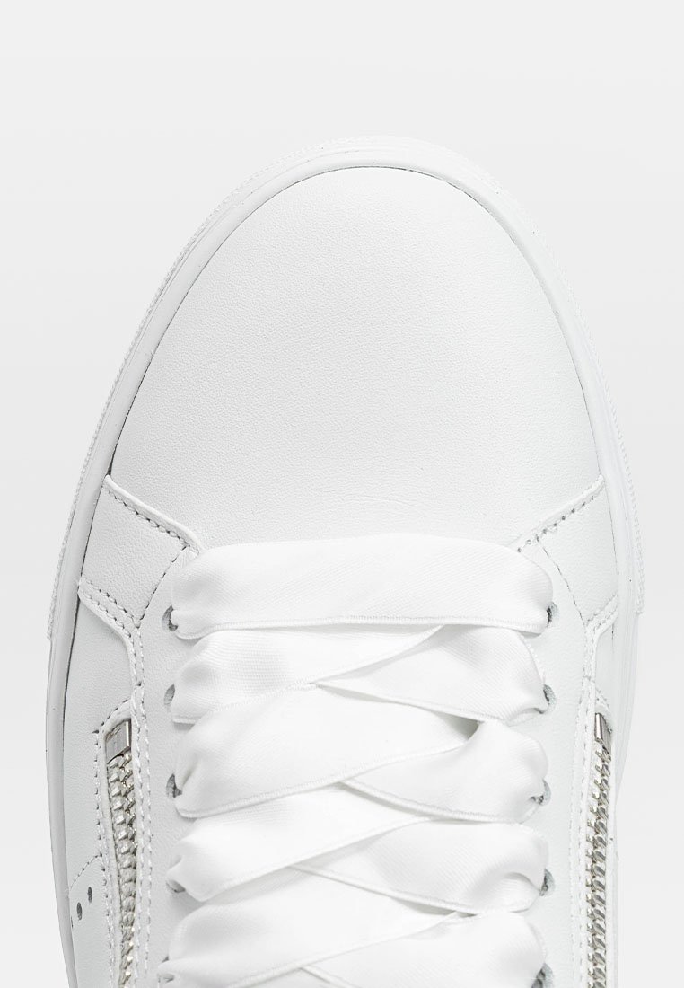 Weiße Sneakers mit einem Obermaterial aus glattem Leder, flachen weißen Schnürsenkeln, seitlichem Reißverschluss und abgerundeter Spitze. Minimalistisches Design mit klaren Linien.