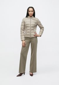 Šviesiai smėlio spalvos dygsniuota striukė su aukštu apykakliu, priekyje užsegama užtrauktuku ir dviem šoninėmis kišenėmis, derinama su alyvuogių žalių plačių kelnių ir aukštakulnių batelių komplektu.