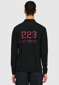 Svart långärmad skjorta med texturerad tyg. Har stora röda siffror "223" och "OFF PITCH" tryckt på ryggen, rund halsdesign.