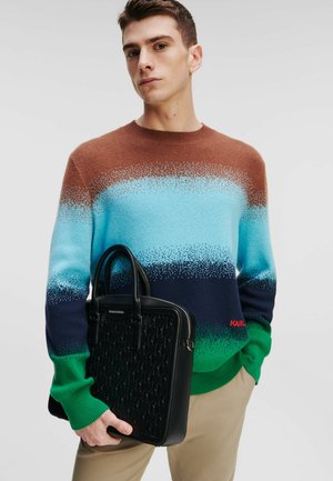 Pull multicolore avec des rayures bleues, vertes et brunes ; tricot texturé ; tenant un sac en cuir noir avec une surface à motifs.