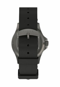Montre Timex avec un bracelet en caoutchouc noir, un boîtier rond et un fond texturé. Elle dispose d'une boucle et d'une barre en argent pour un maintien sécuritaire.