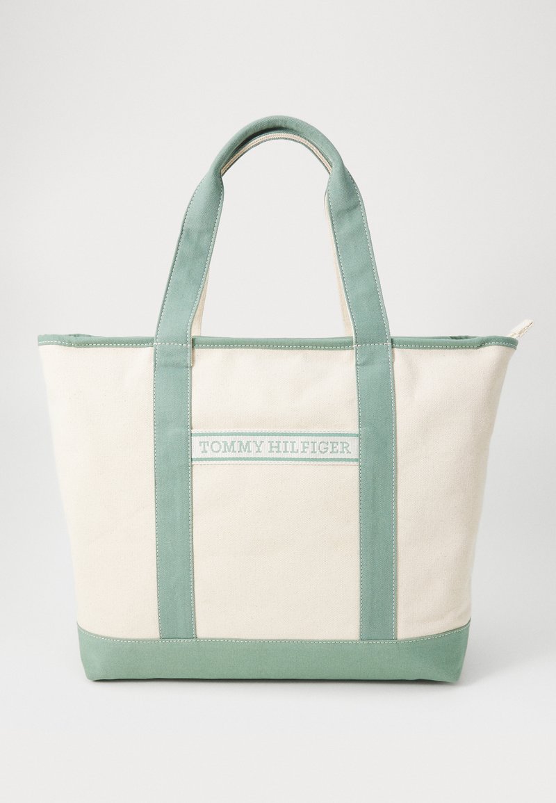 Canvas tote bag in cream with mint green accents, featuring a flat base, dual handles, and a logo patch on the front.