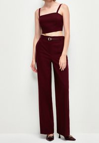 Burgundy tvådelad outfit med en figurnära crop top med tunna band och högmidjade, vida byxor med bältesdetalj.