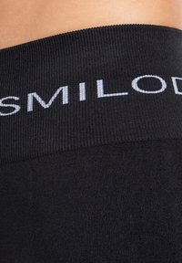 Fascia elastica nera con texture a coste, con la scritta "SMILODON" in caratteri bianchi. Il tessuto appare liscio ed elastico.