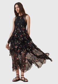 Black tiered dress made of sheer fabric with floral pattern, featuring a lace bodice, flowing layers, and a knee-length hem. Black sandals included.
