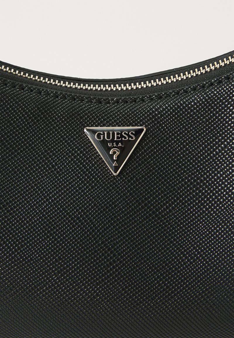 Schwarze, strukturierte Handtasche mit einem dreieckigen Metall-Logo-Schild, auf dem "GUESS U.S.A." geprägt ist, und einem Reißverschluss in goldfarbener Optik entlang der oberen Kante.