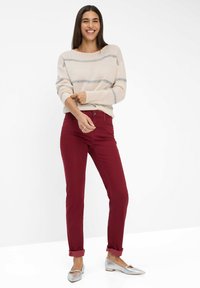 Gestreifter Creme-Pullover, bordeauxfarbene Hose, silberne Ballerinas. Der Pullover hat eine lockere Passform und gerippte Bündchen; die Hose ist tapered mit aufgerollten Säumen.