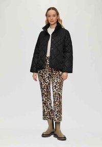 Zwart gewatteerd jack met een hoge kraag en knoopsluiting, gecombineerd met een broek met panterprint in beige, bruin en zwart, en grijze enkellaarsjes.